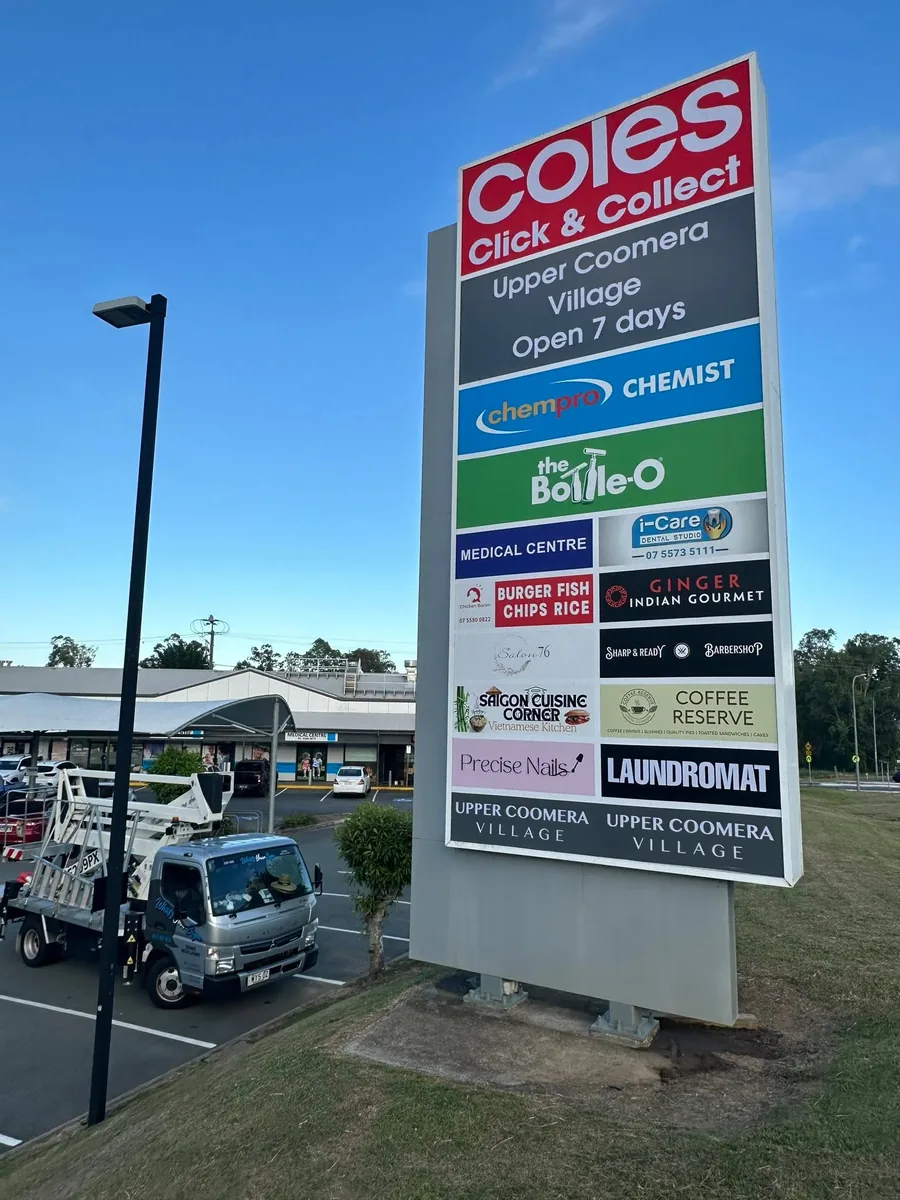 Tall multi tenant pylon sign at dusk with Coles Click and Collect at the top and specialty tenant panels below