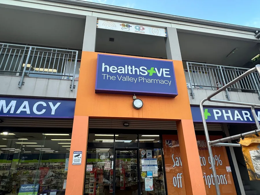 Illuminated purple lightbox sign for healthSAVE The Valley Pharmacy mounted above a shopfront entry