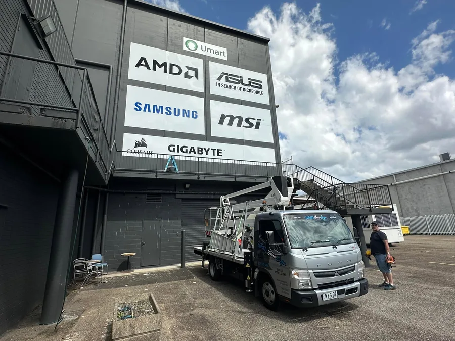 Truck mounted elevated work platform parked below a two storey facade carrying six installed brand panels